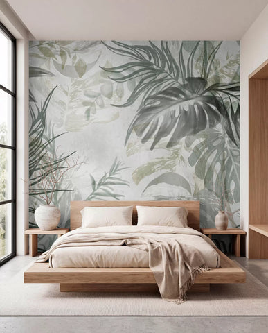 Monstera and palm leaves wall mural in soft green and grey behind a low wooden bed