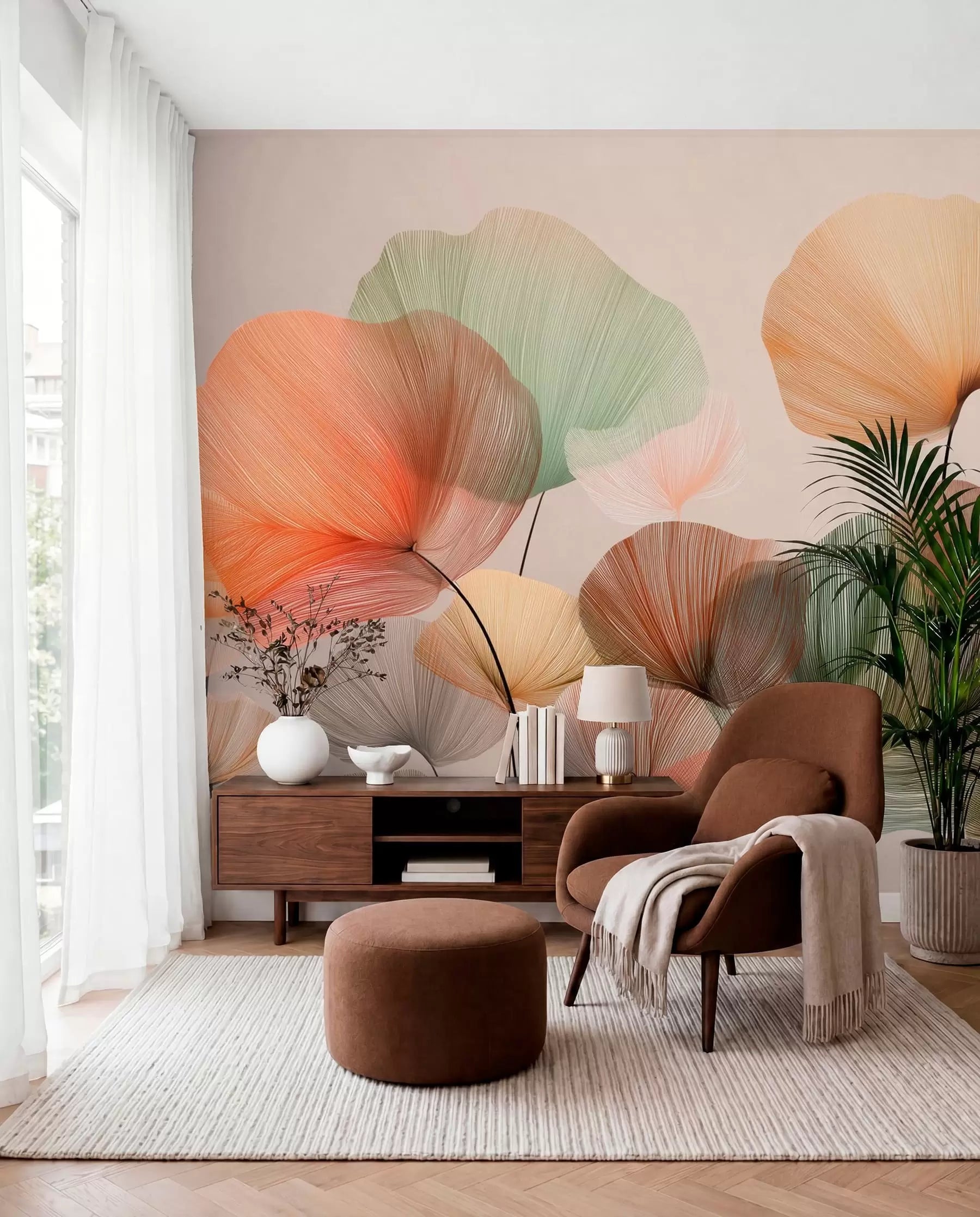 Multicoloured ginkgo leaves wall mural in coral, sage and peach behind a brown armchair and sideboard