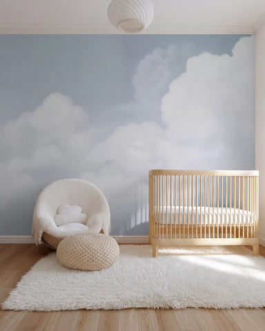 Painted blue sky and white clouds wall mural in a nursery with a wooden crib and boucle chair