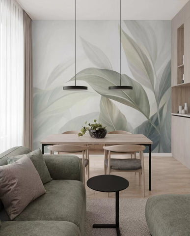 Soft sage green tropical leaves wall mural in an open-plan dining area with a green sofa